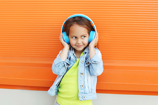 Happy child enjoys listens to music in headphones over orange background