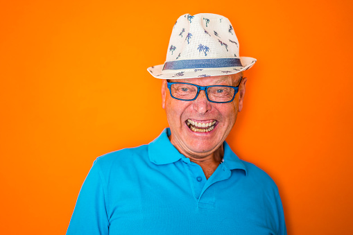 crazy laughing 70 year old senior man with hat and glasses in color surge theme with colorful background