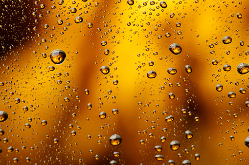 Ice cold glass  covered with water drops condensation  Cold drink Drops of water Golden yellow - orange drink background Raindrops texture Close up